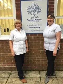 Two of the practice team in clinic uniform outside the Wantage Podiatry sign at Little Orchard House